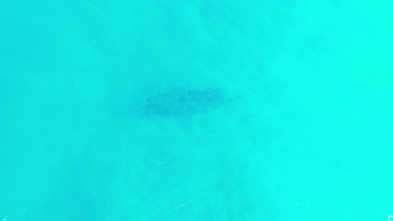 Turquoise shallow sea seen from above with faint darker underwater patches.