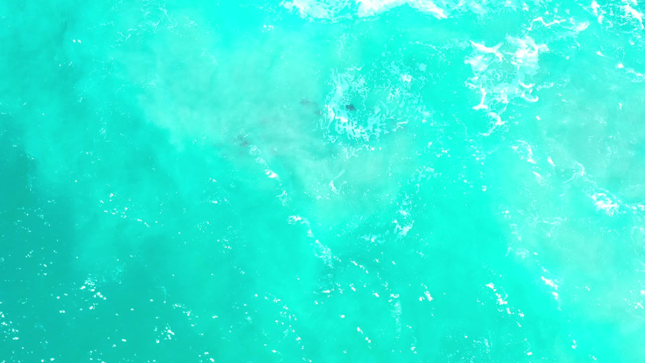 Overhead turquoise ocean water in Los Cabos, Mexico, with scattered white foam near the upper edge and no visible people.