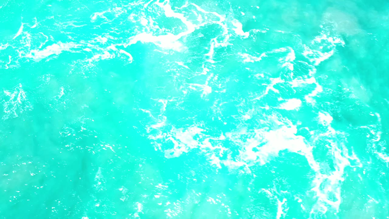 Bright blue ocean water in Los Cabos with a loose white foam patch near the center and no visible people.