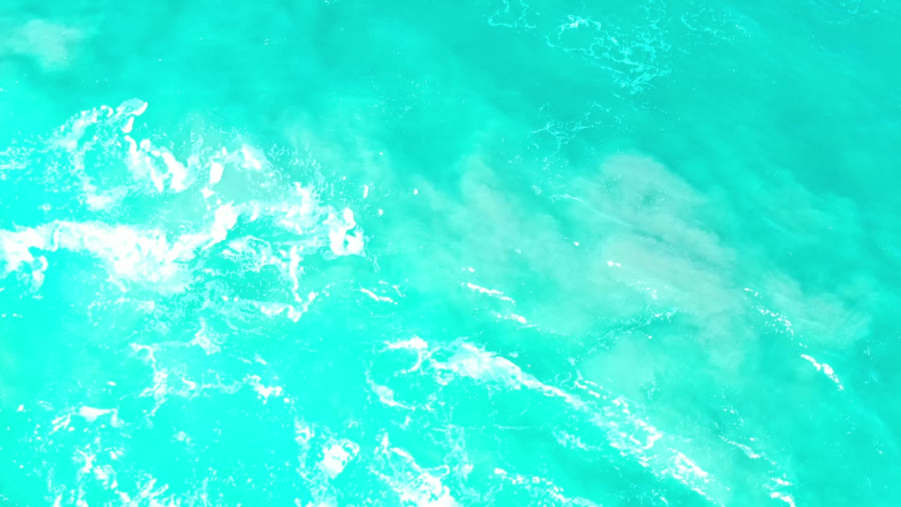 Turquoise sea surface with white foam and faint underwater contours.