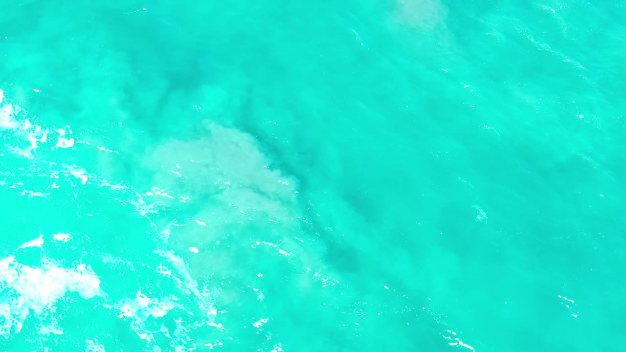 Turquoise ocean surface with white foam and pale underwater patches.