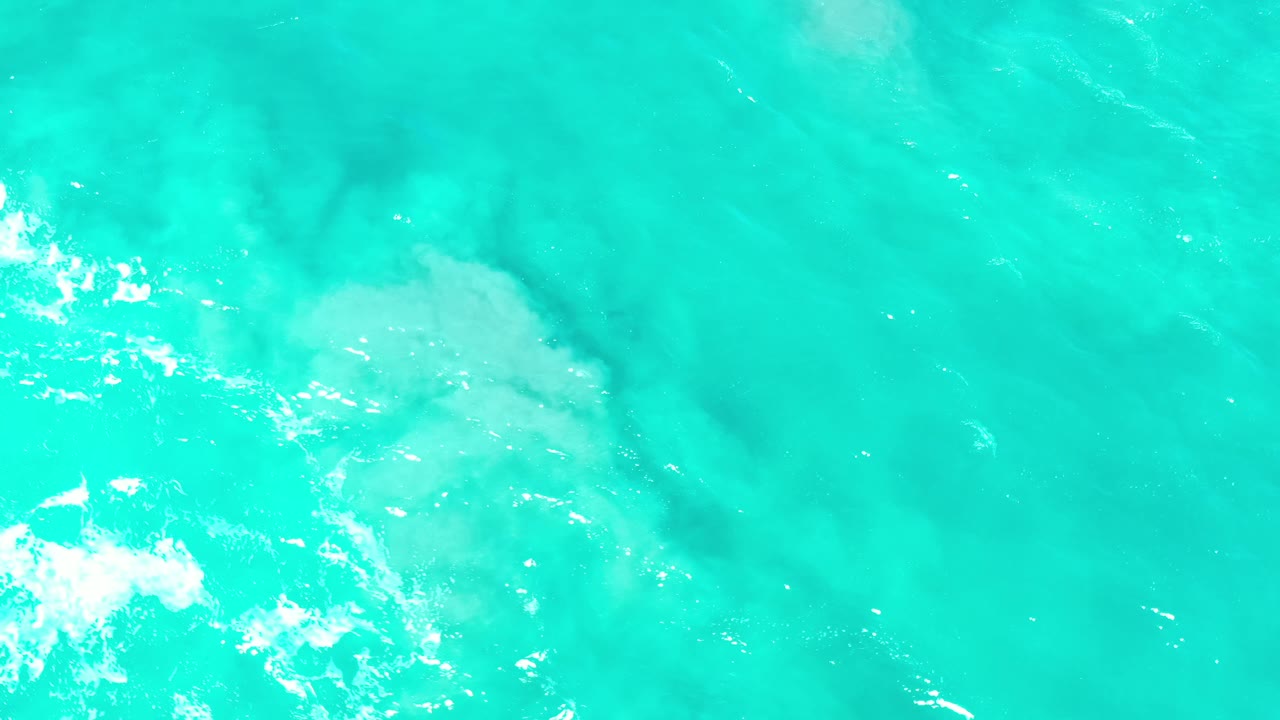 Overhead Los Cabos ocean frame with teal water, small white wave breaks, and no visible people or vessels.