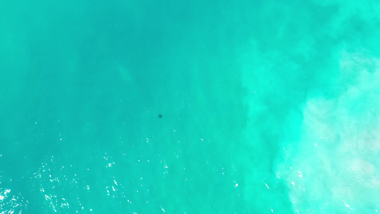 Top-down turquoise seawater with pale sandy clouding beneath the surface.
