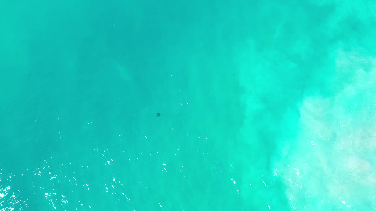 Overhead Los Cabos water frame with scattered bright reflections near the lower edge, faint submerged sand texture, and no visible people.
