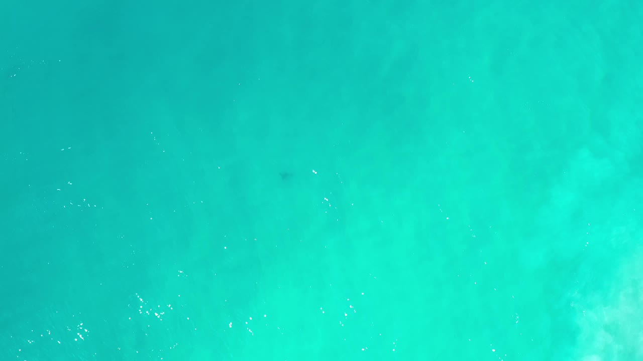 Clear aqua water in Los Cabos, Mexico, seen from above with scattered white sunlight glints and no visible people.