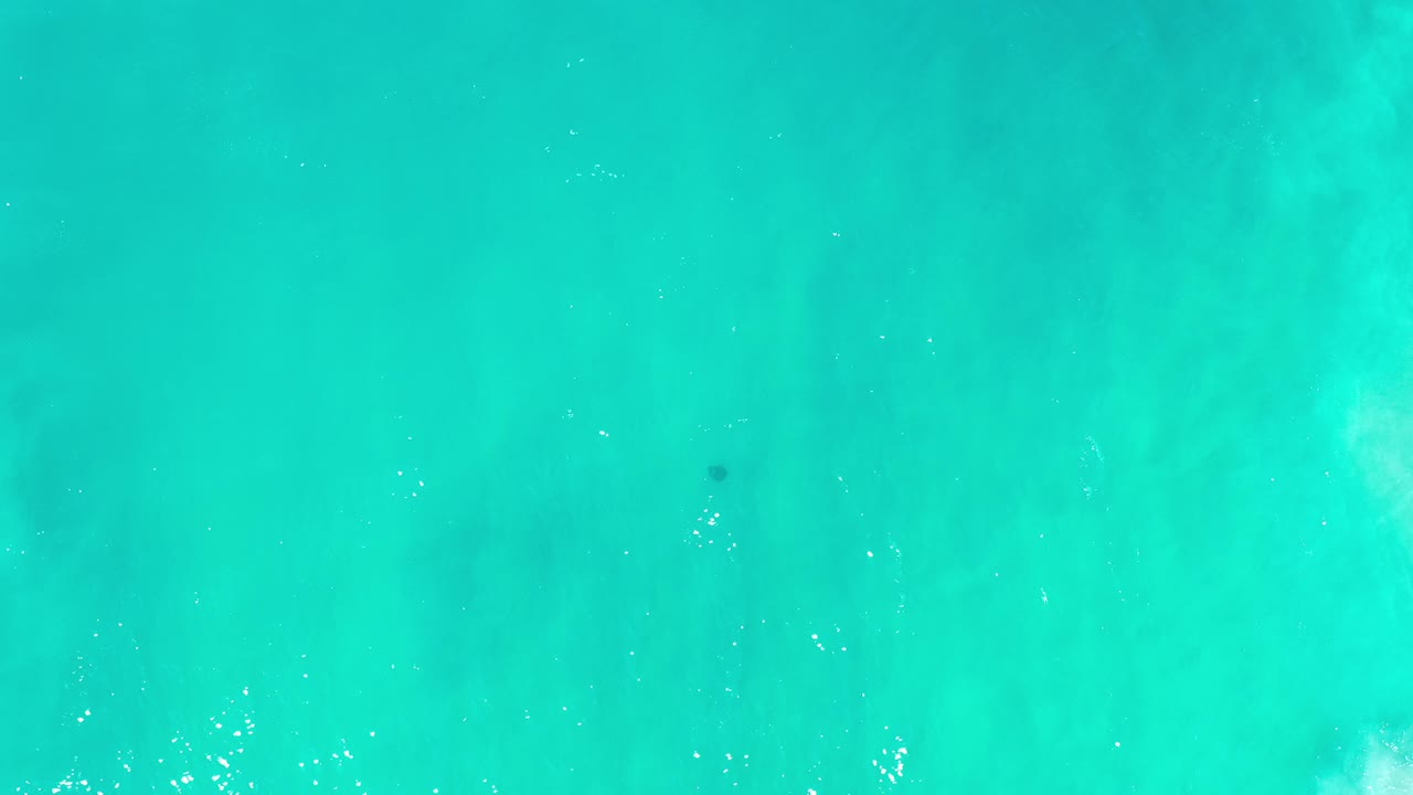 Turquoise water with scattered foam and a dark underwater spot.