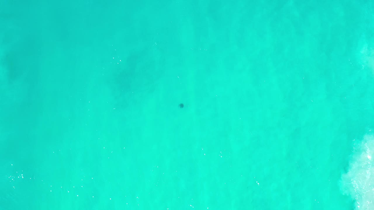 Overhead view of teal ocean water in Los Cabos, Mexico, with faint foam near the right side and no visible people.