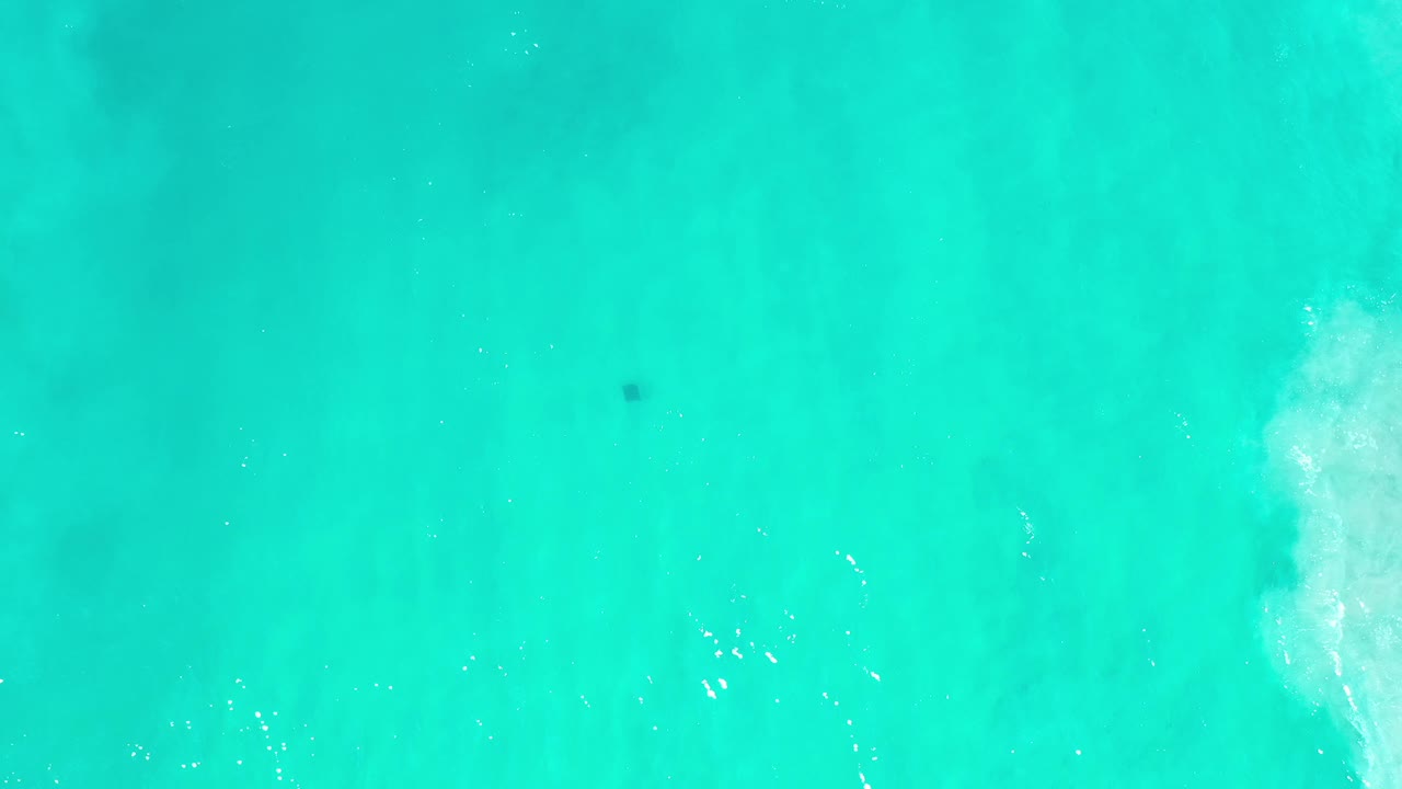 Overhead Los Cabos water frame with a faint dark patch below the surface, scattered sun glints, and no visible people.