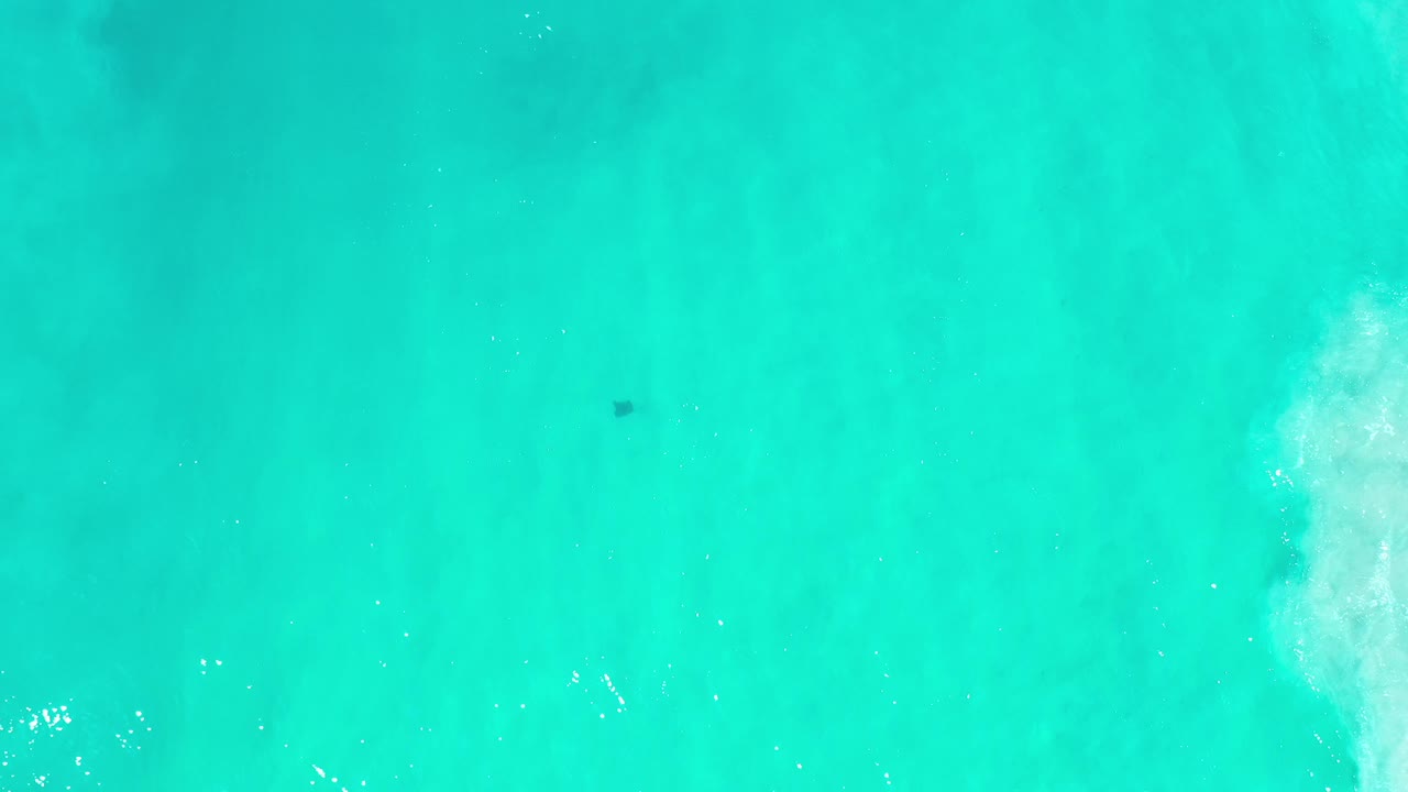 Clear turquoise water with white wave foam along the right edge
