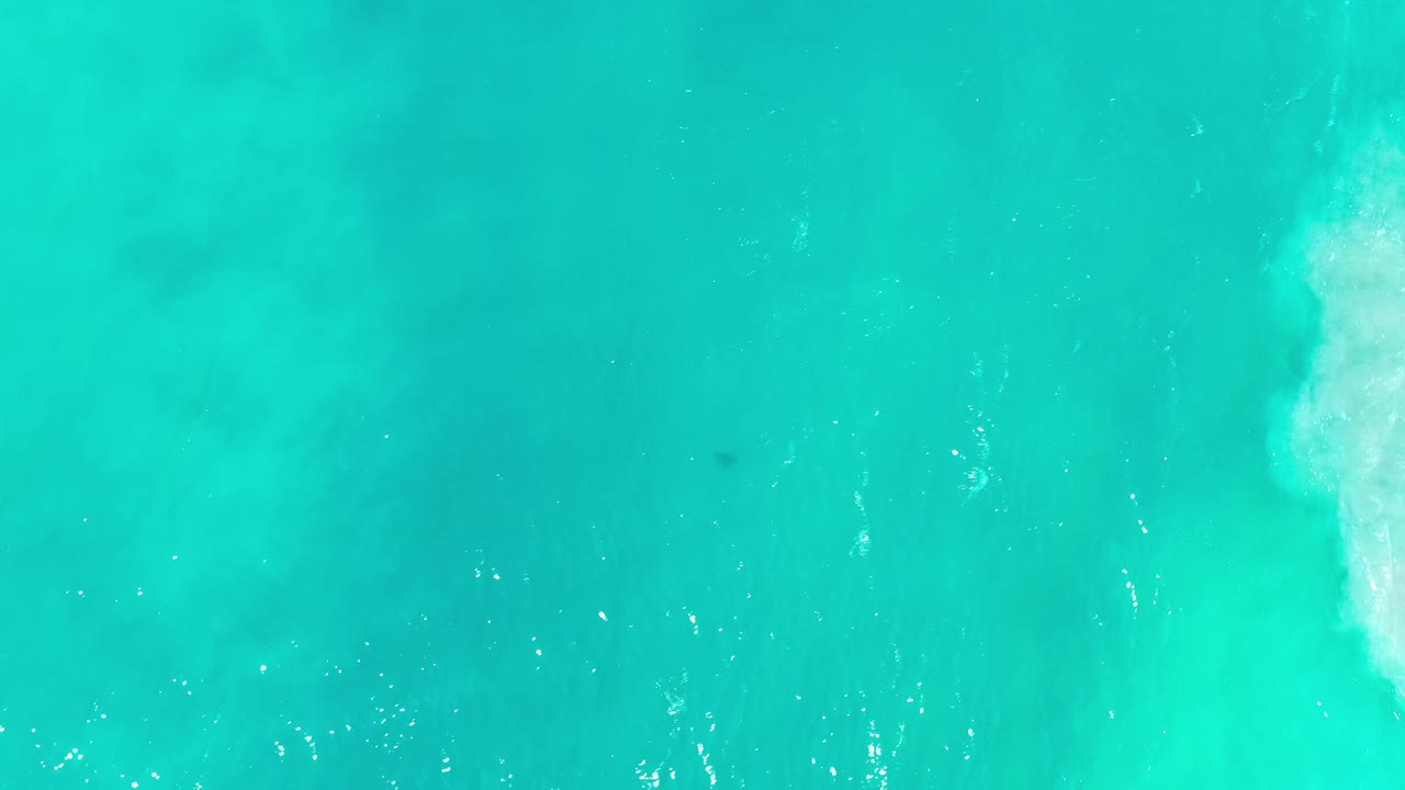 Overhead Los Cabos ocean frame showing green-blue water, faint darker underwater patches, scattered surface sparkle, and no visible people.
