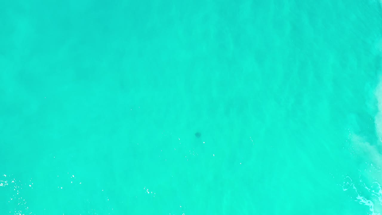 Overhead 4K view of turquoise ocean water in Los Cabos, Mexico, with pale underwater bands near the right side and no visible people.