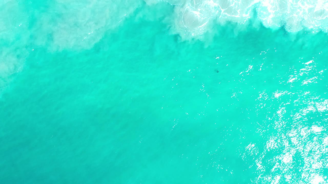 Aqua water fills the frame in Los Cabos as foamy wave wash spreads across the upper edge, with no visible people.