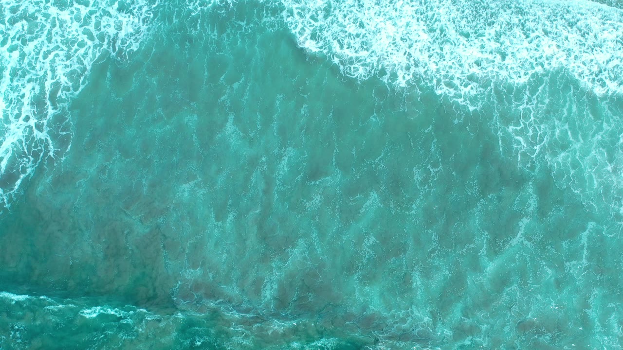 Top-down view of turquoise ocean surf in Los Cabos, Mexico, with white foam spread across the upper edge and no visible people.