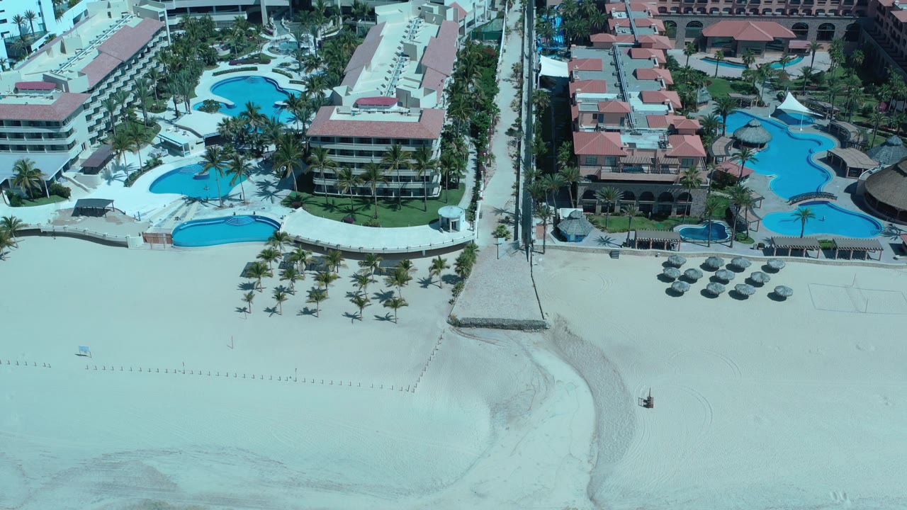 Overhead resort view with beach, pools, and hotel roofs.
