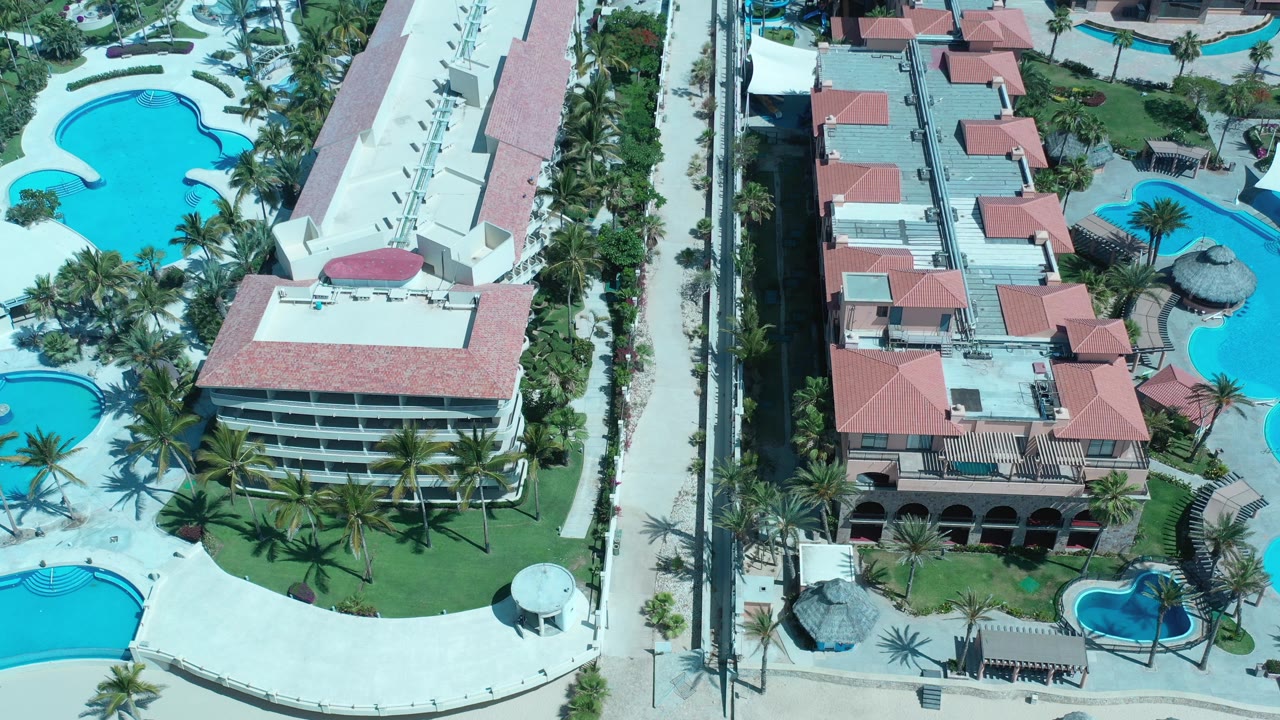 Aerial view of red-roofed buildings, pools, palms, and walkways.