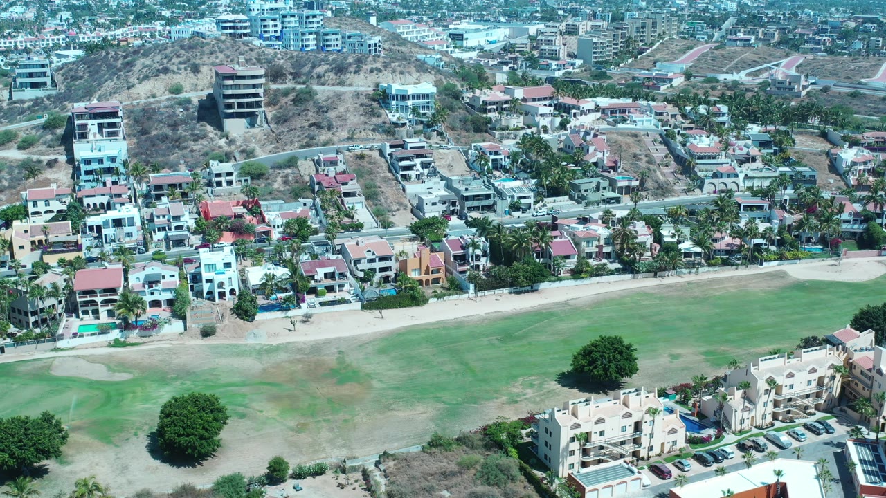 Elevated view of apartments, houses, palm trees, sandy ground, and green turf.