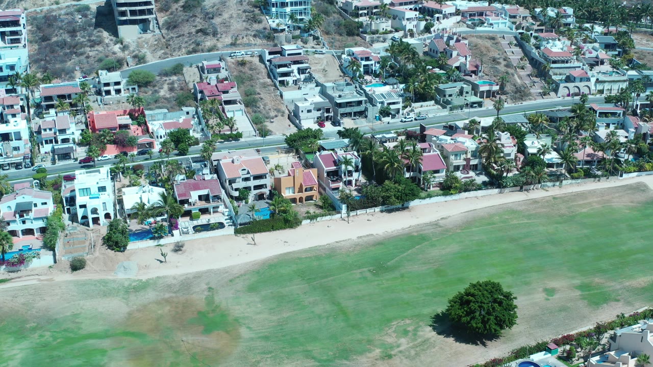 Aerial view of homes, road, sandy strip, and green field.
