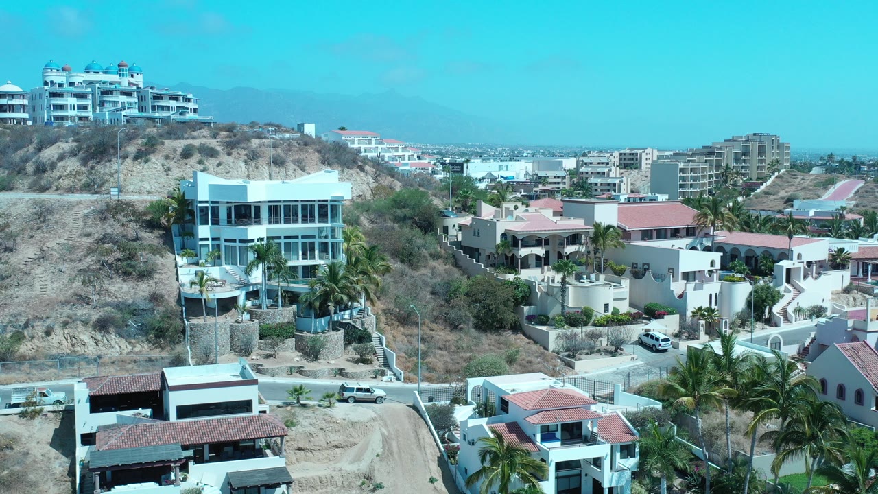 Elevated view of hillside homes, palms, mountains, and distant ocean.