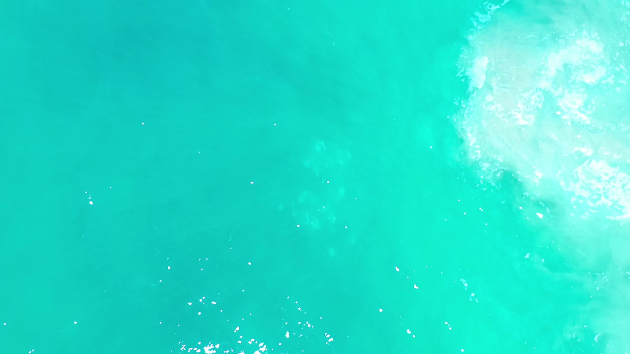 Turquoise sea surface with white foam near the upper right.