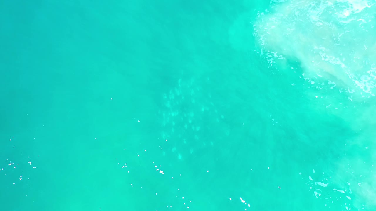 Overhead Los Cabos water frame showing blue-green surface texture, faint white foam at the top edge, and no visible people.