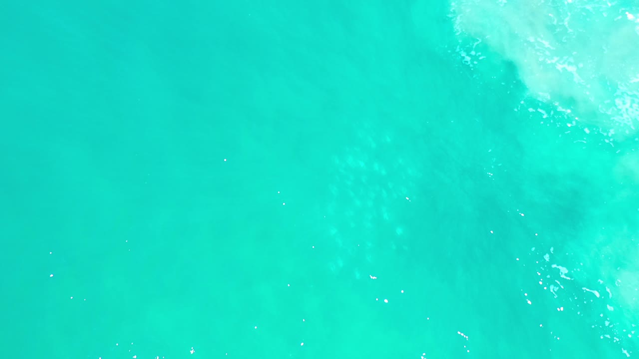 Overhead view of bright teal ocean water in Los Cabos, Mexico, with soft white wash entering near the upper right and no visible people.