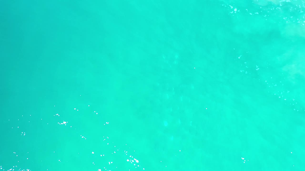 Bright aqua Los Cabos ocean water shows scattered white sparkle points and soft cloudlike patches below the surface, with no visible people.