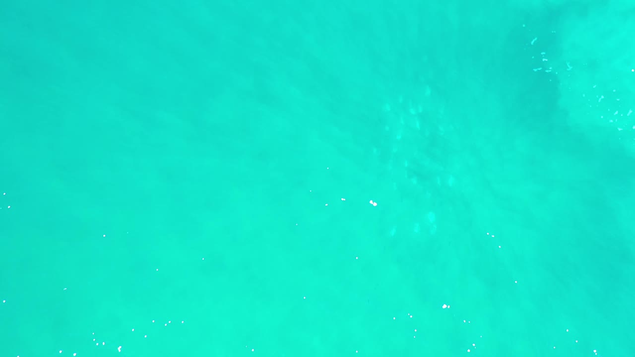 Bright overhead view of green-blue ocean water in Los Cabos, Mexico, with scattered white glints and no visible people.