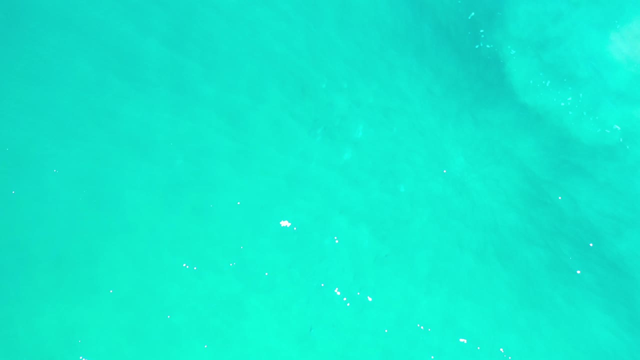 Direct overhead view of turquoise sea in Los Cabos, Mexico, with faint darker water patches and no visible people.