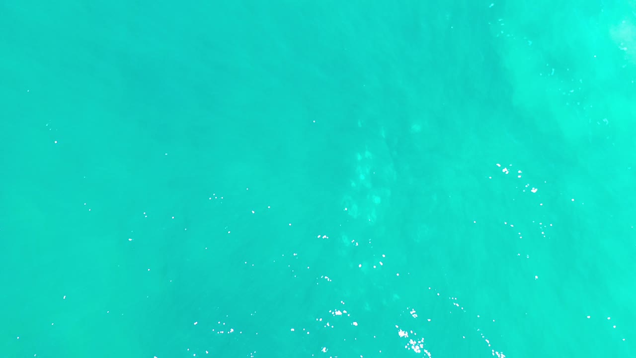 Top-down view of turquoise sea water in Los Cabos, Mexico, with faint cloud shadowing and no visible people.