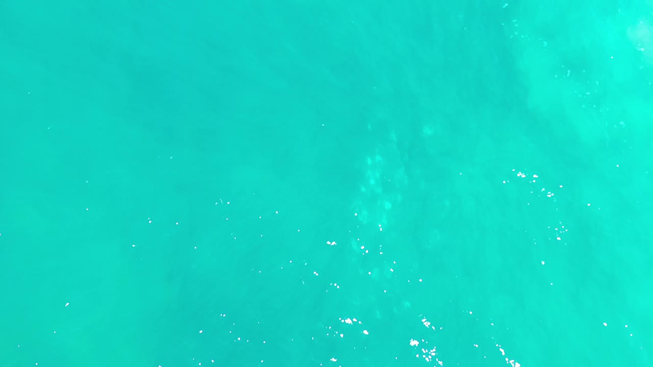 Overhead Los Cabos sea surface with slightly darker blue patches crossing the turquoise water and no visible people.