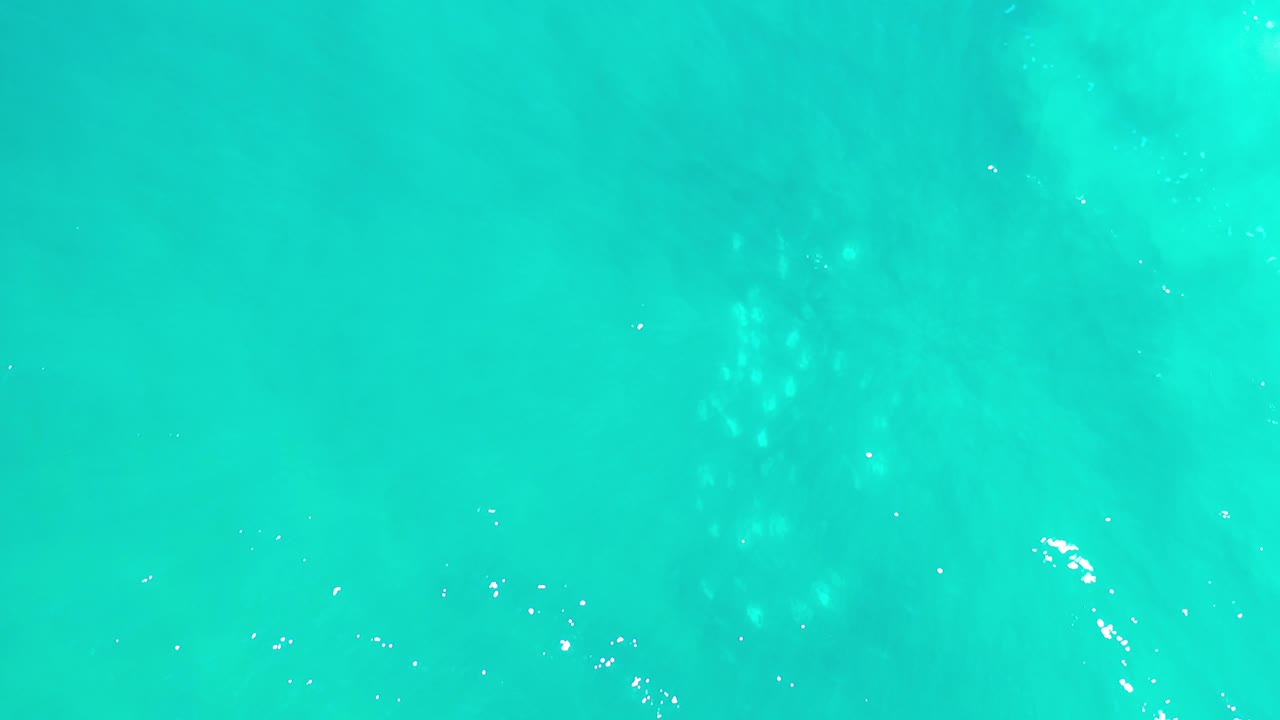 Aerial view of bright turquoise water and white sparkle marks.