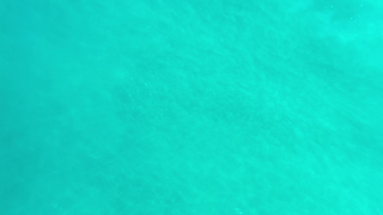 Turquoise water in Los Cabos, Mexico fills the frame at the opening moment, with soft ripples, pale underwater texture, and no visible people.