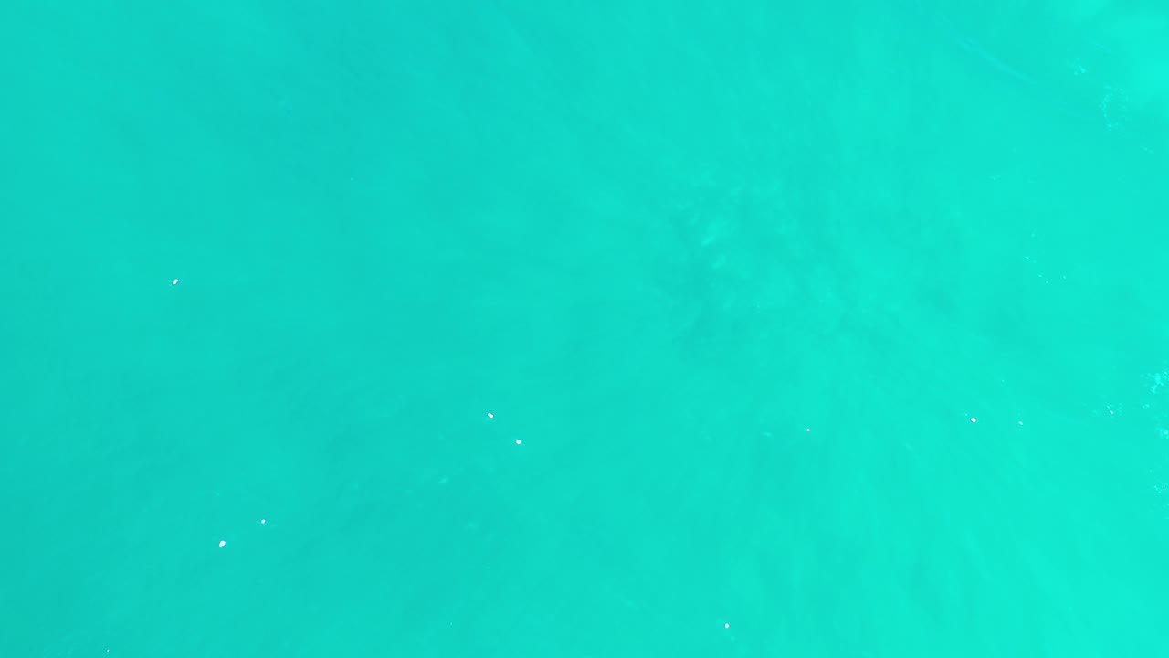 Bright turquoise sea water fills the opening frame in Los Cabos, Mexico, with faint darker patches below the surface and no visible people.