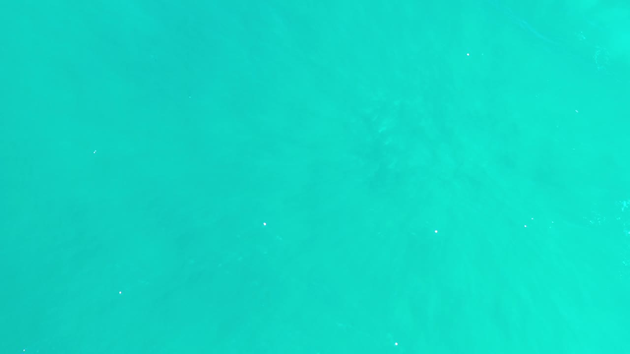Green-blue ocean water fills the frame in Los Cabos, Mexico, with scattered white light flecks and no visible people.