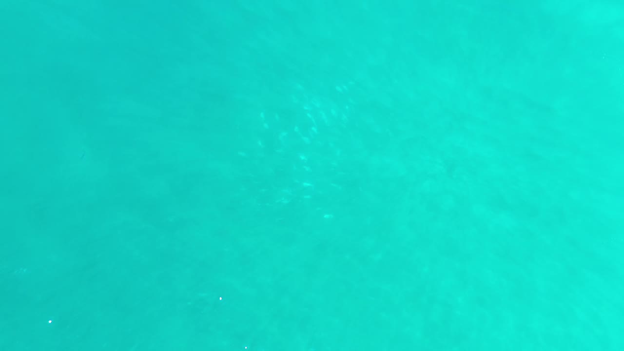 Clear blue-green Los Cabos water shows scattered white highlights across an otherwise empty frame, with no visible people.