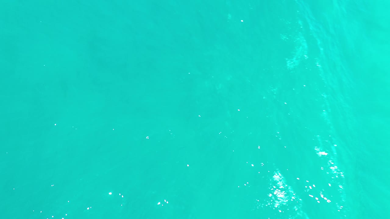 Turquoise ocean surface with small white sun glints.