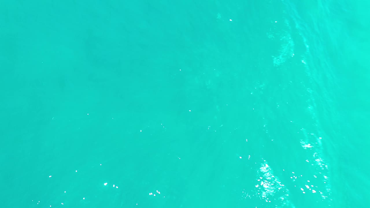Overhead Los Cabos ocean frame showing blue-green water, pale underwater tonal shifts, scattered sparkle highlights, and no visible people.