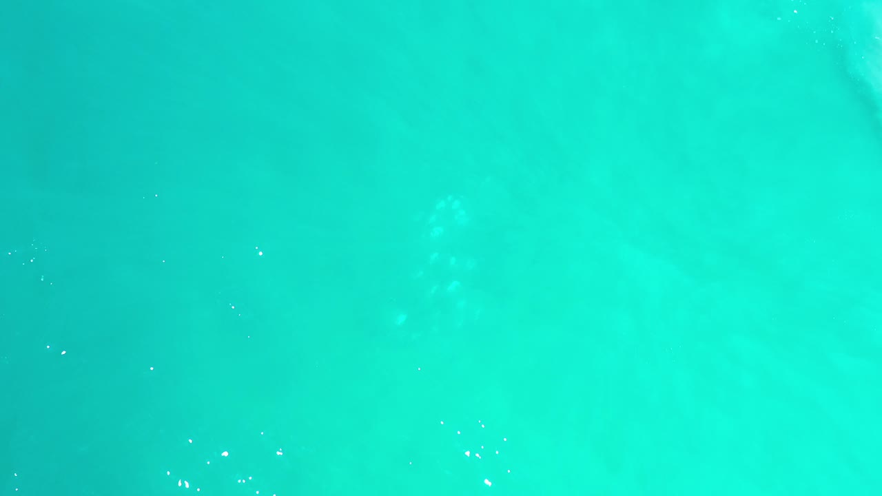 Overhead view of turquoise sea water in Los Cabos, Mexico, with faint pale wave bands and no visible people.