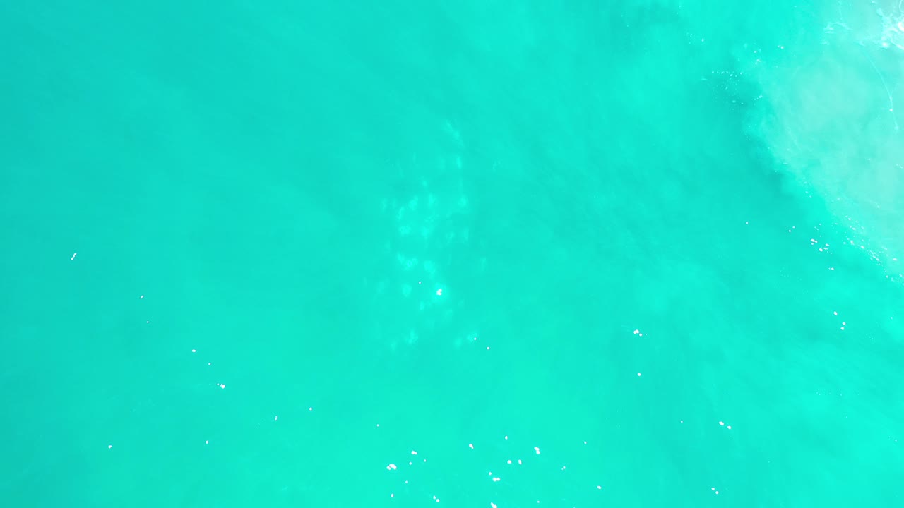 Overhead view of green-blue sea water in Los Cabos, Mexico, with faint pale wave streaks near the upper right and no visible people.