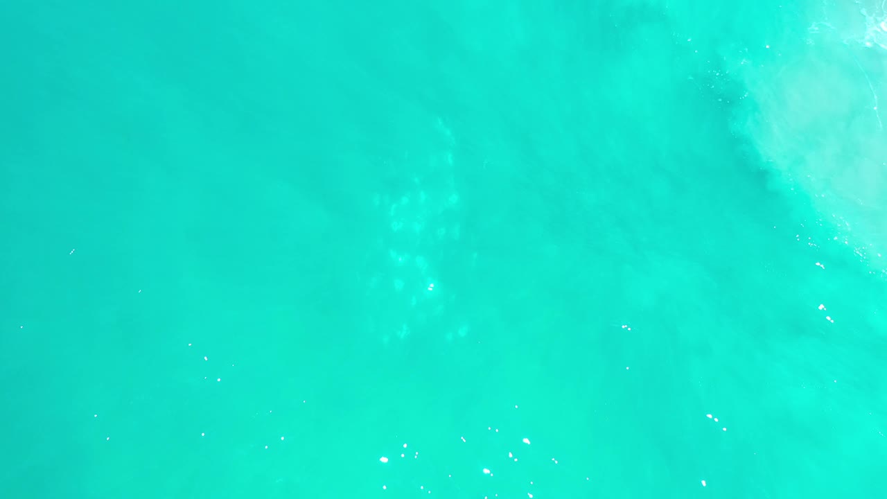 Green-blue Los Cabos sea water fills the frame, with scattered white sun glints and subtle cloudy wave patterns, no visible people.