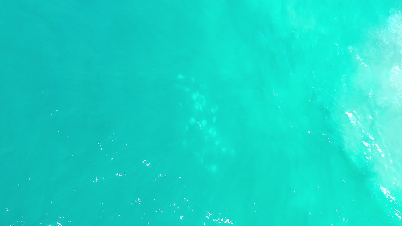 Overhead view of clear turquoise ocean water in Los Cabos, Mexico, with faint sand visible below and no visible people.