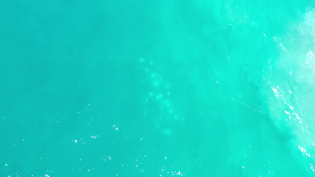 Clear blue-green ocean water in Los Cabos, Mexico, with a brighter wave streak crossing the right side and no visible people.
