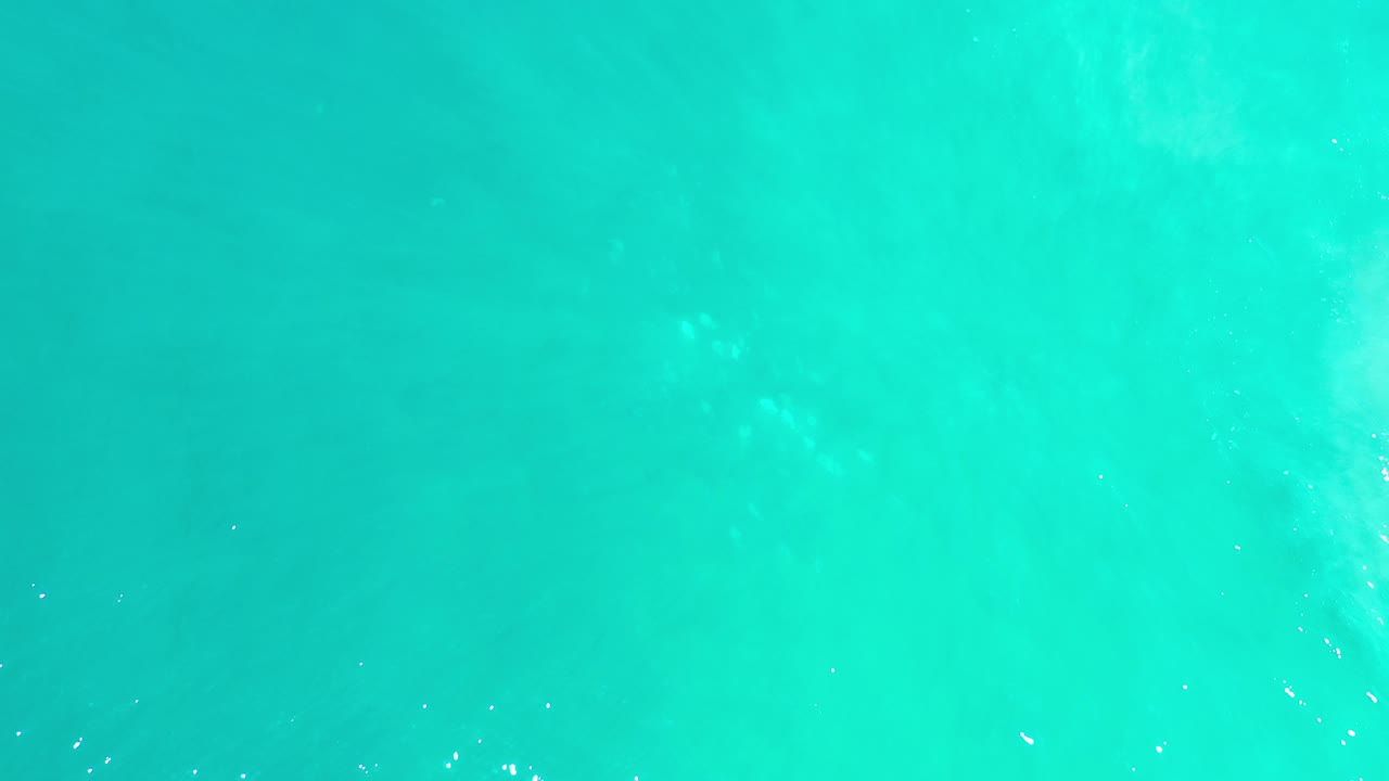 Top-down view of bright turquoise sea water in Los Cabos, Mexico, with faint cloudy shallows and no visible people.