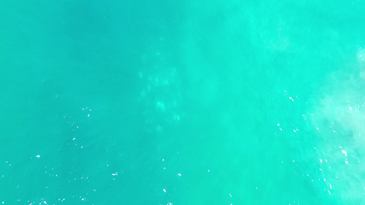 Overhead view of clear teal ocean in Los Cabos, Mexico, with a pale wave patch forming near the middle and no visible people.
