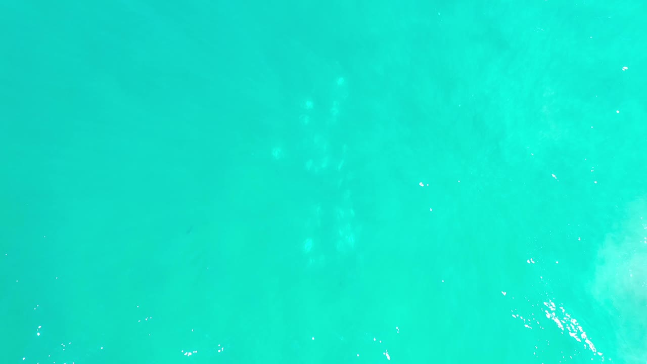 Blurred turquoise water in Los Cabos, Mexico, with small bright flecks near the upper part of the frame and no visible people.