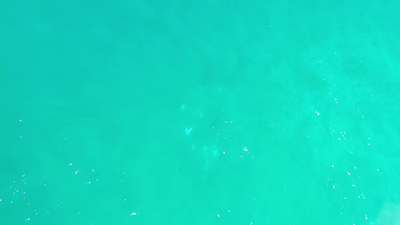 Aerial view of bright turquoise ocean in Los Cabos, Mexico, with scattered light ripples and soft color variation across the water, no visible people.