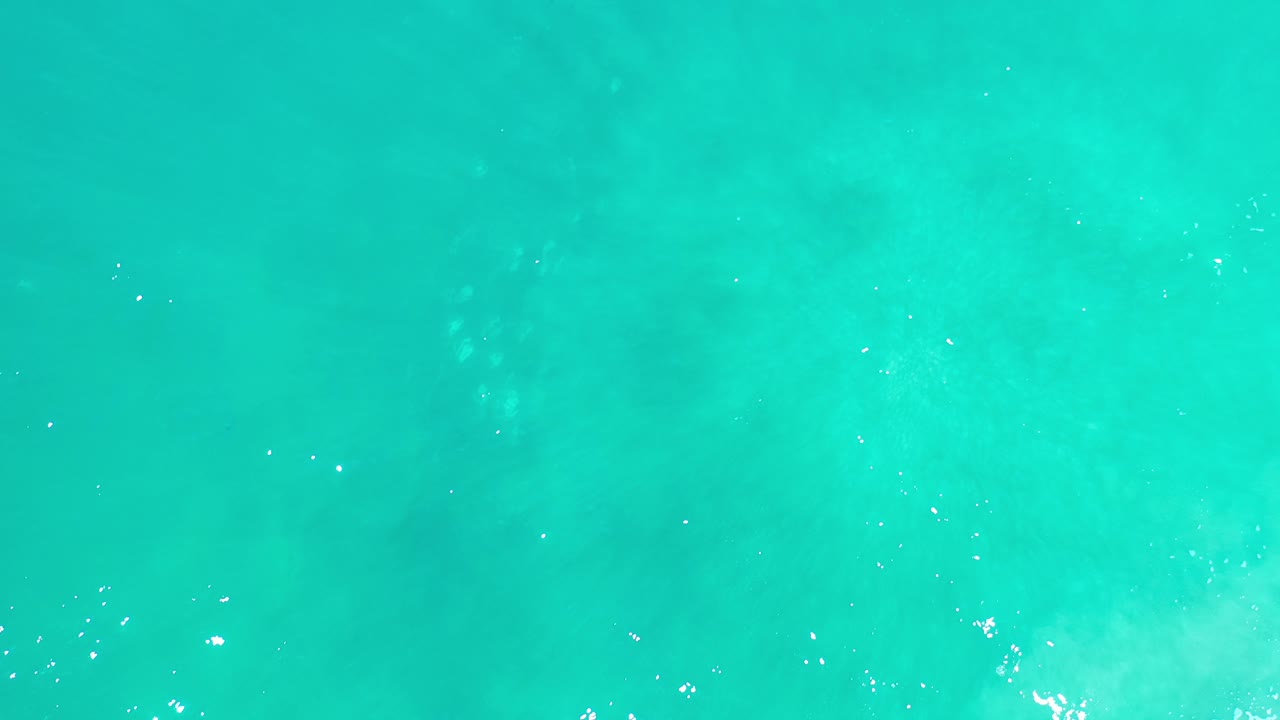 Overhead view of turquoise clear water in Los Cabos, Mexico, with scattered bright reflections near the surface and no visible people.