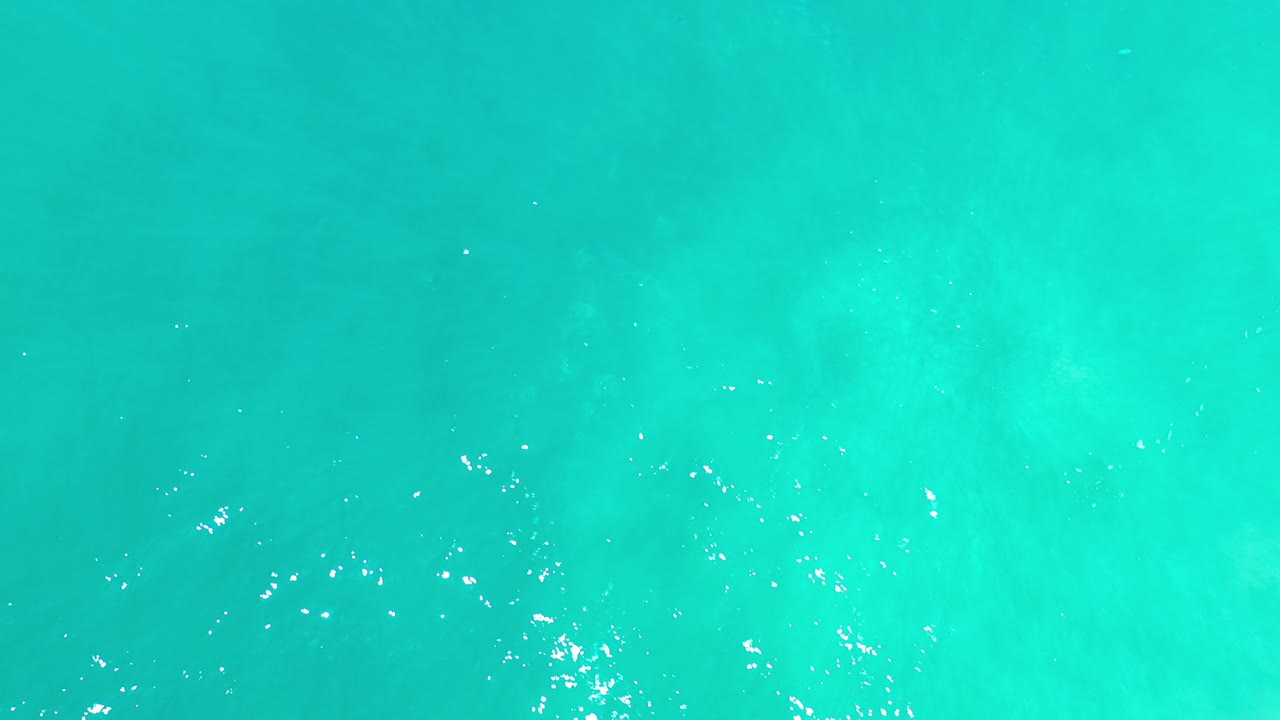 Turquoise-green sea water in Los Cabos fills the frame at the start of the clip, with scattered white reflections and no visible people.