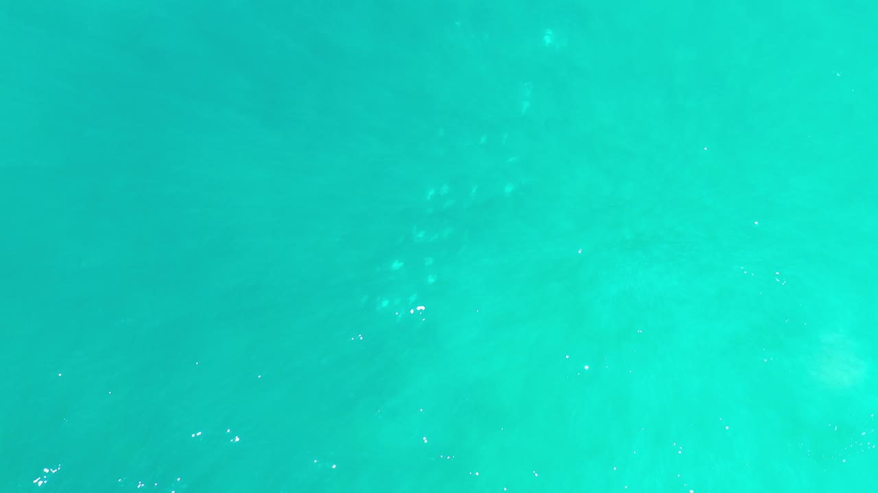 Turquoise-green sea surface with faint white foam specks.