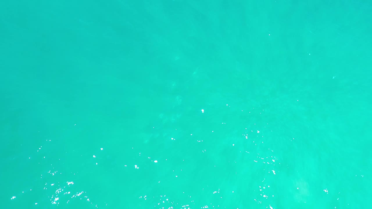 Aqua ocean water in Los Cabos appears slightly brighter across the frame, with scattered sun sparkle and soft tonal variation below the surface, with no visible people.
